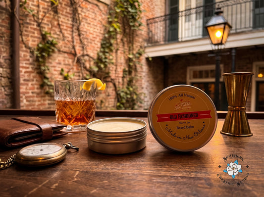 Old Fashioned beard balm by Southern Creative Studio, open tin and lid with a French Quarter courtyard bar with a Sazerac-style cocktail and gas lantern