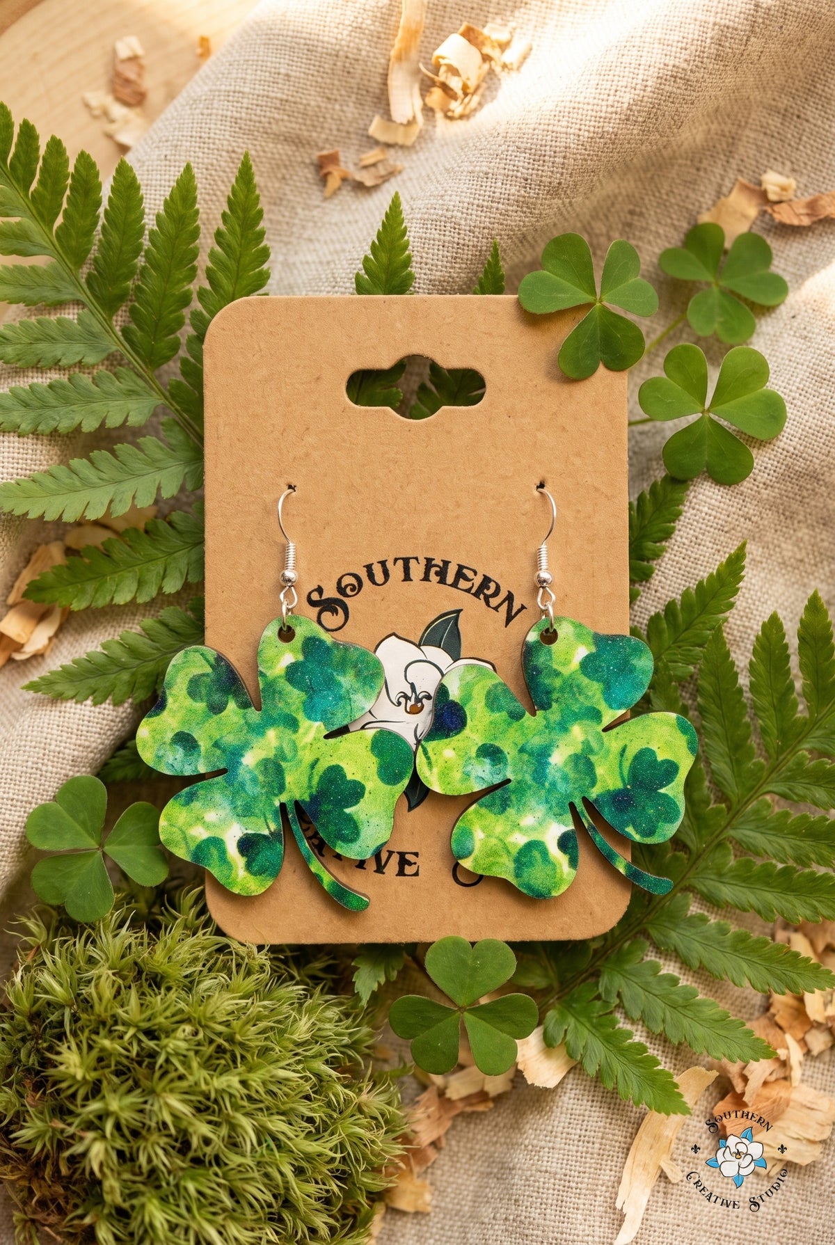 Marbled four leaf clover earrings on card in a fern and shamrock flat lay