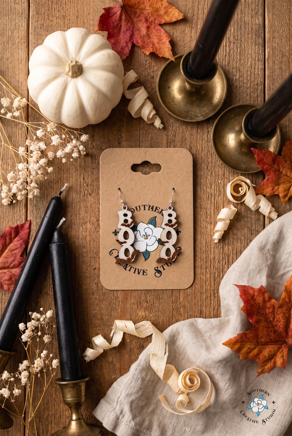 BOO bat earrings on card flat lay with Halloween pumpkin, candles and autumn leaves