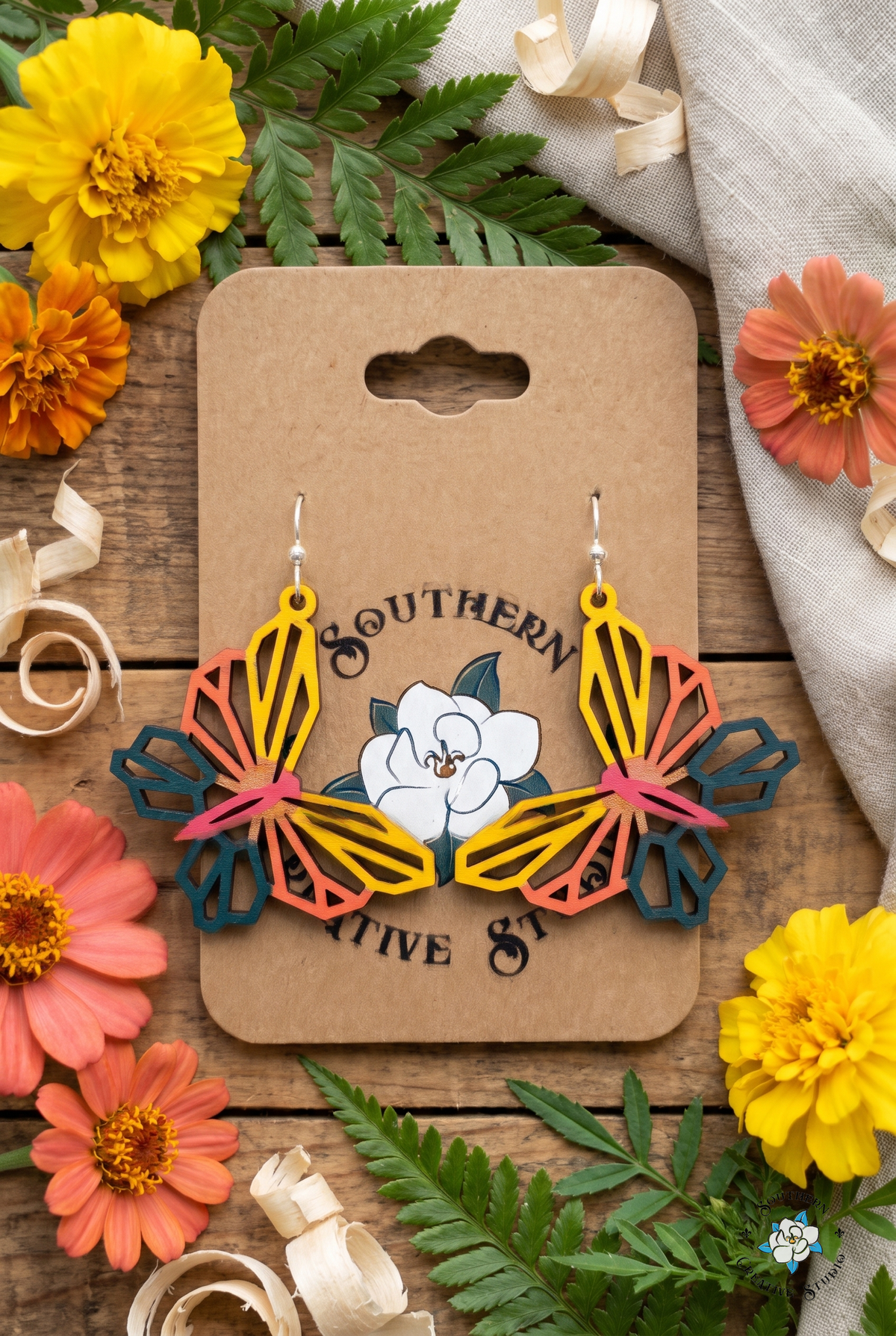 Yellow and coral geometric butterfly earrings flat lay with marigolds and zinnias on kraft card