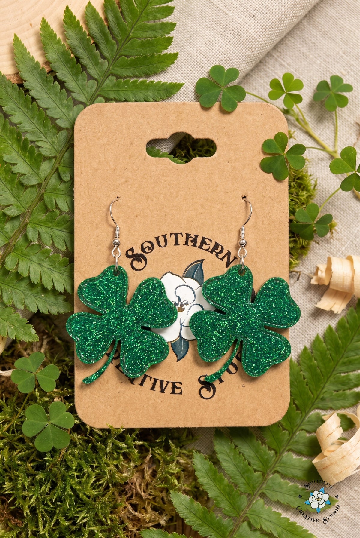 Four leaf clover earrings on card in a fern and shamrock flat lay