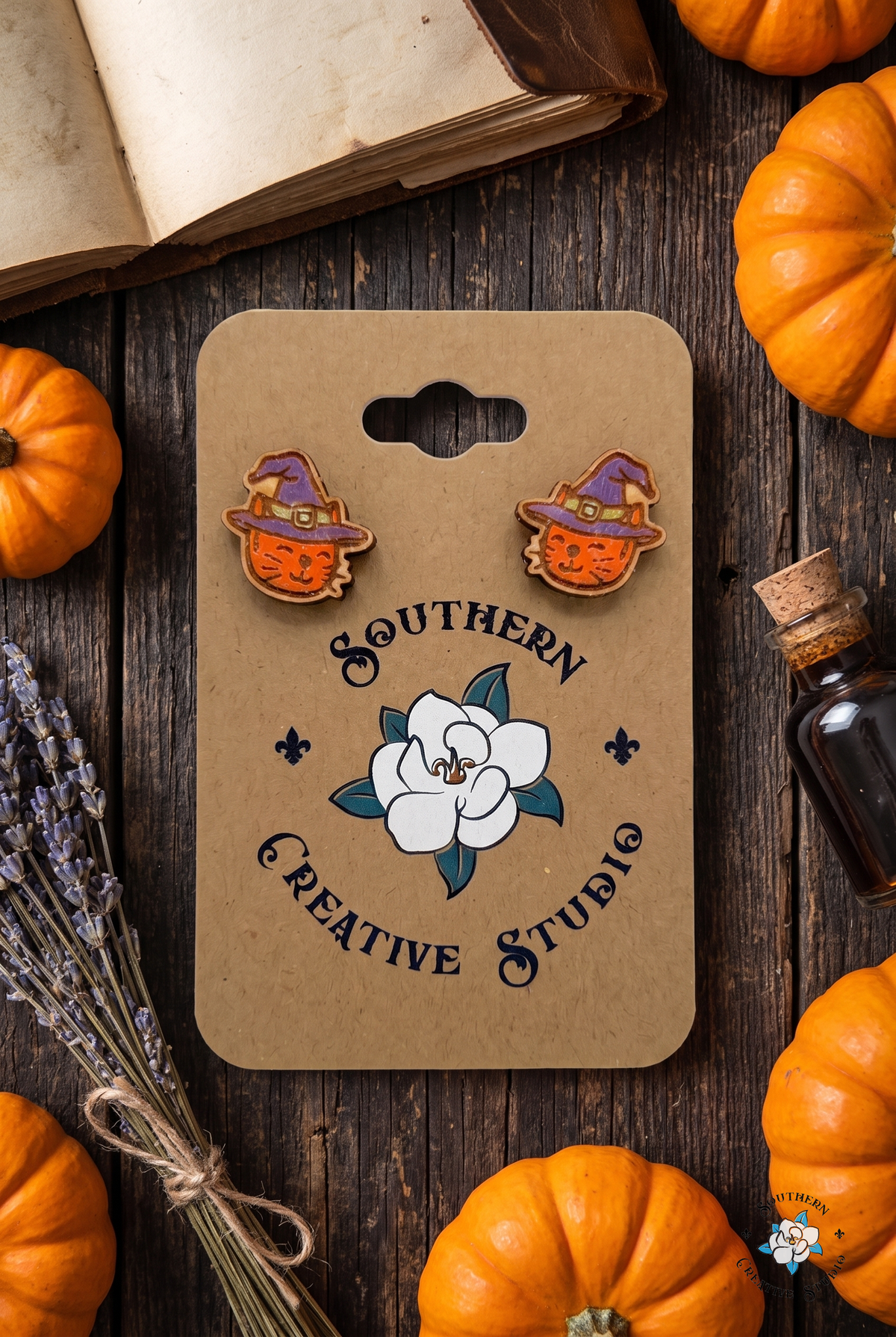 Flat lay of witch cat stud earrings on SCS card with spellbook, pumpkins and lavender
