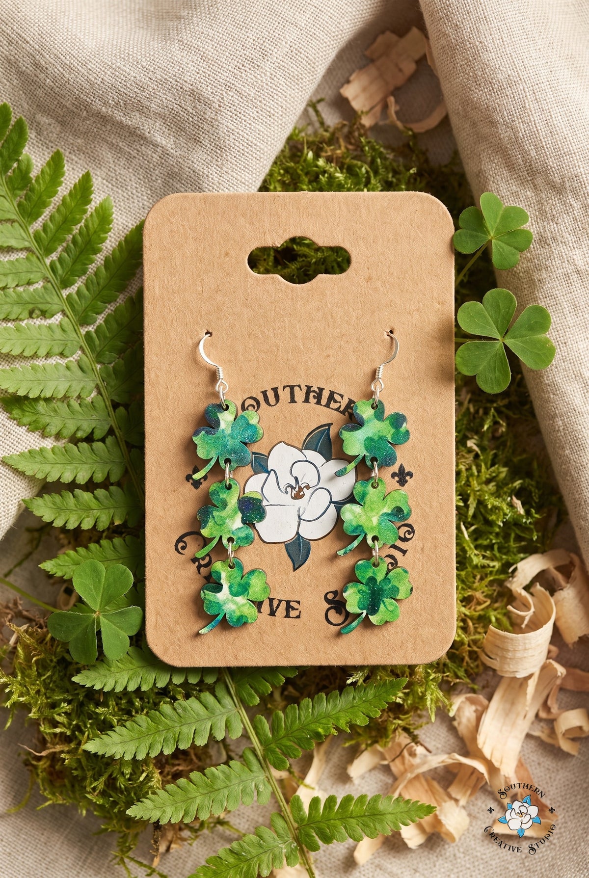 Four leaf clover dangle earrings on card in a fern and shamrock flat lay