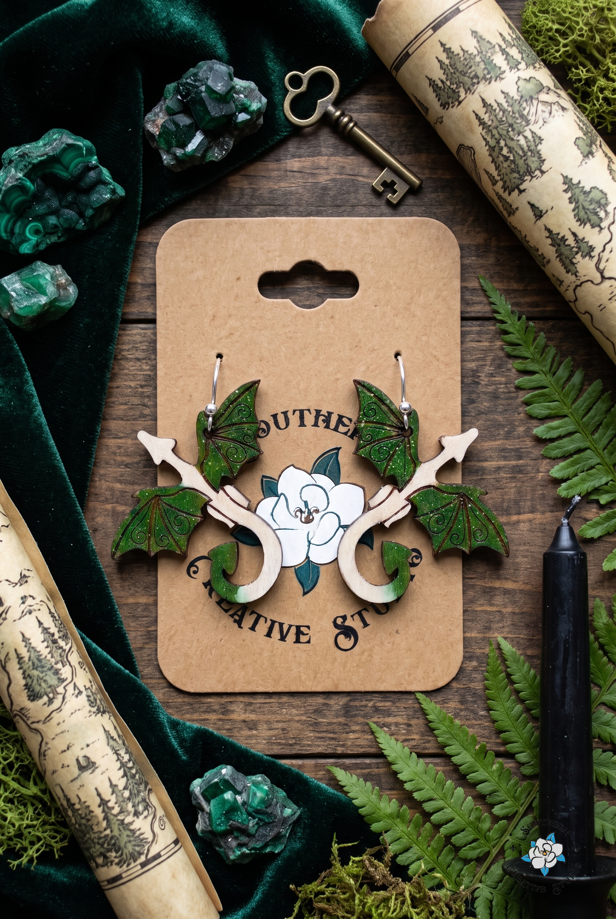 Flat lay of forest green dragon earrings on SCS card with green velvet, malachite, brass key, forest map and ferns