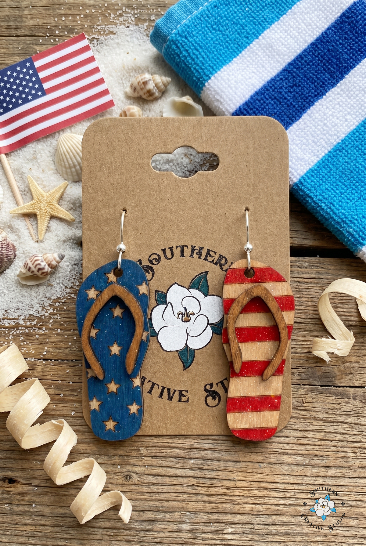 USA flip flop earrings flat lay with sand, starfish and mini flag on kraft card