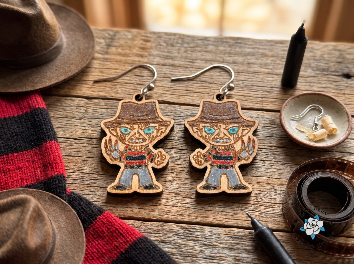 Hand-painted slasher wood earrings on rustic table with red-and-black striped sweater, fedora and film strip