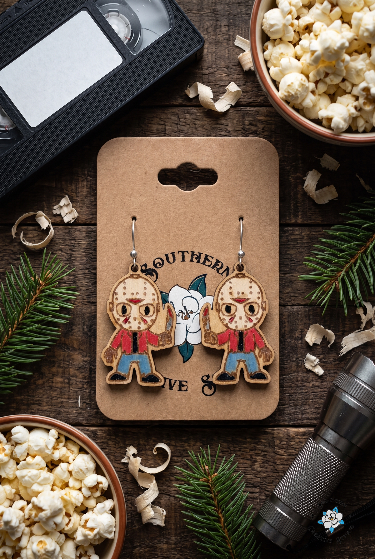 Horror movie night flat lay with slasher earrings on hang card, popcorn and pine