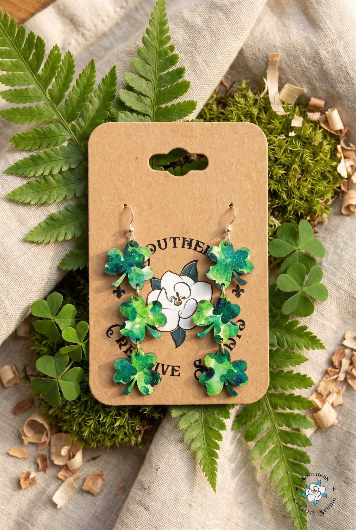Three leaf clover dangle earrings on card in a fern and shamrock flat lay
