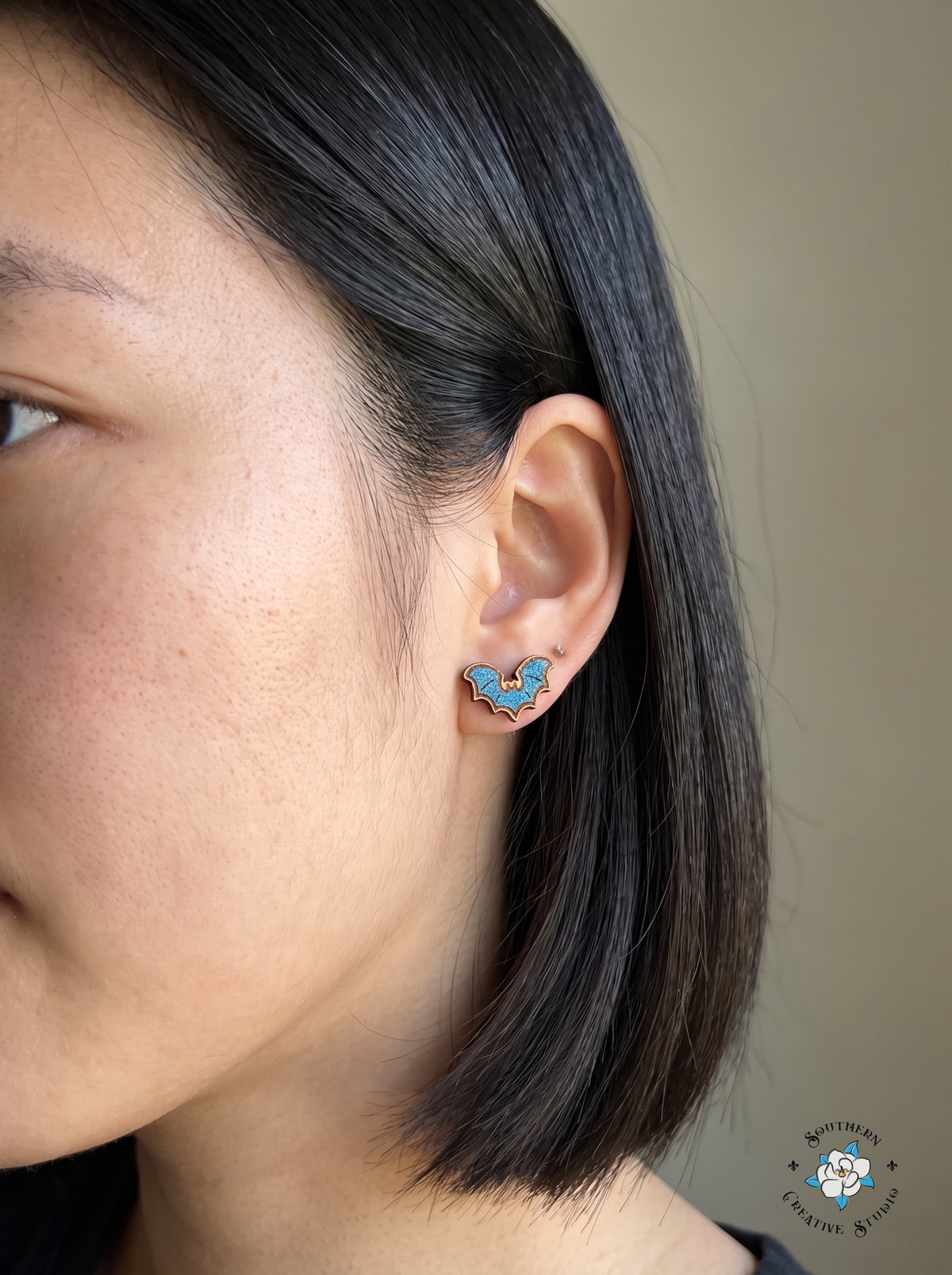 Close-up of blue bat wood stud earring worn in ear