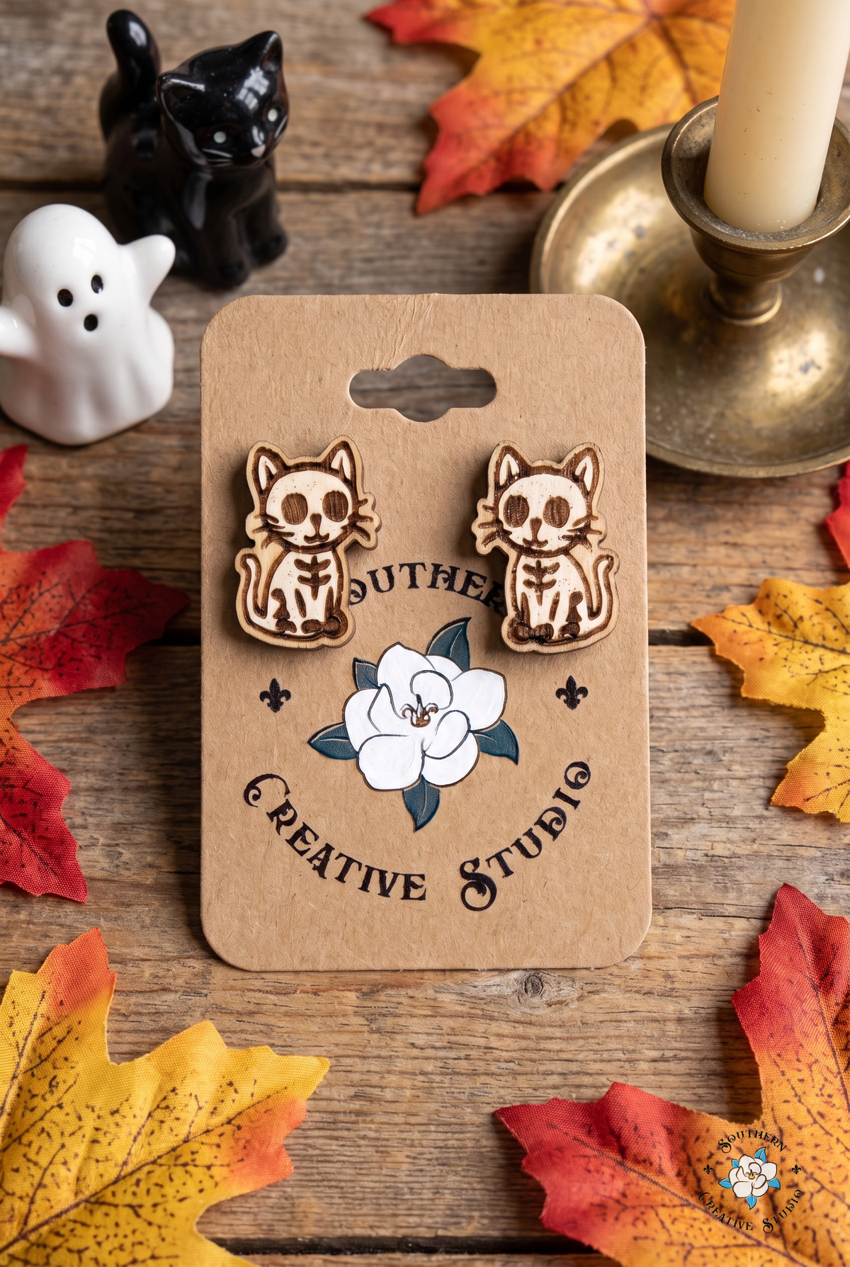 Flat lay of skeleton cat stud earrings on SCS card with black cat, ghost and autumn leaves