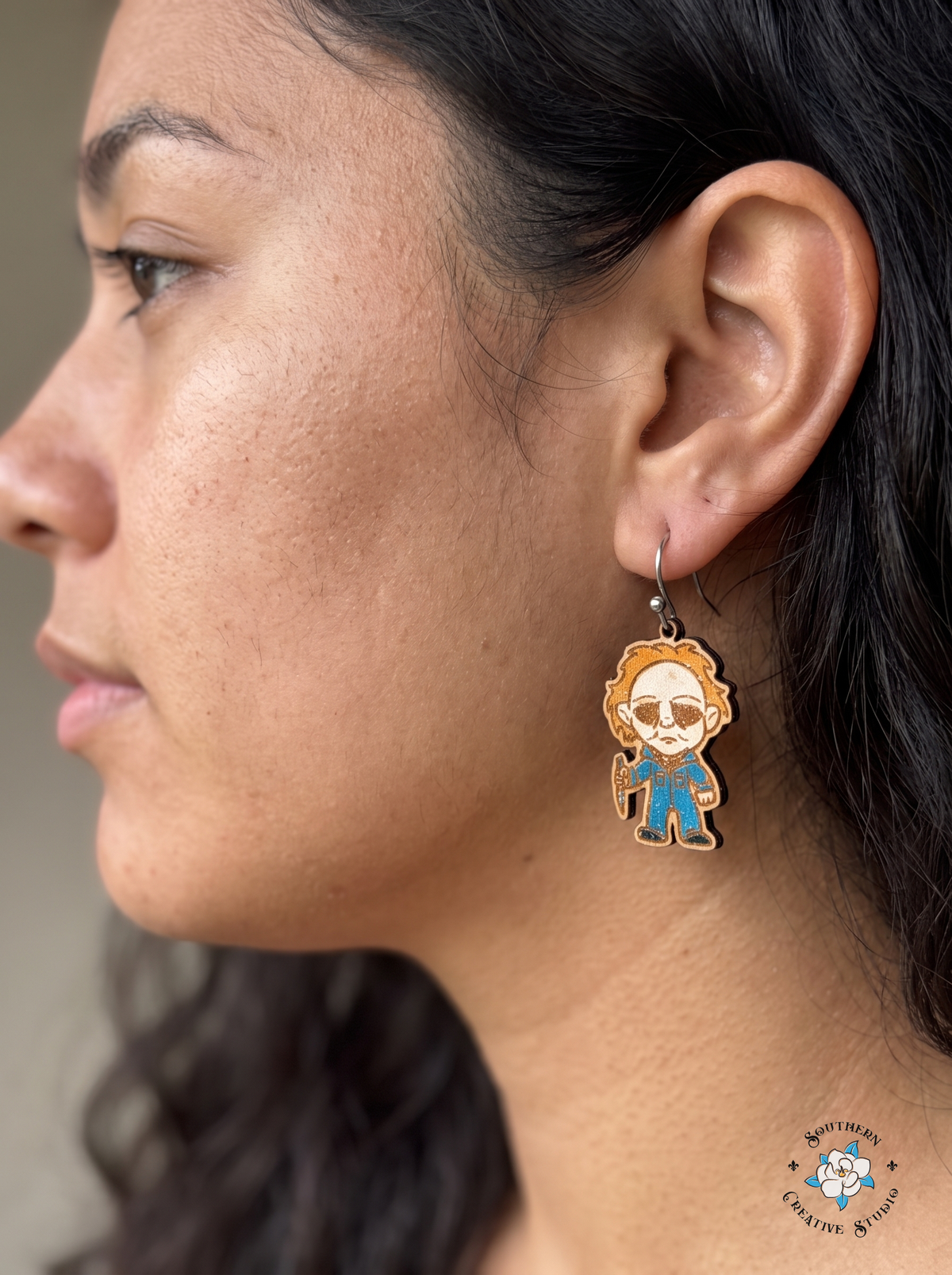 Woman wearing masked slasher chibi wood earring in blue coveralls
