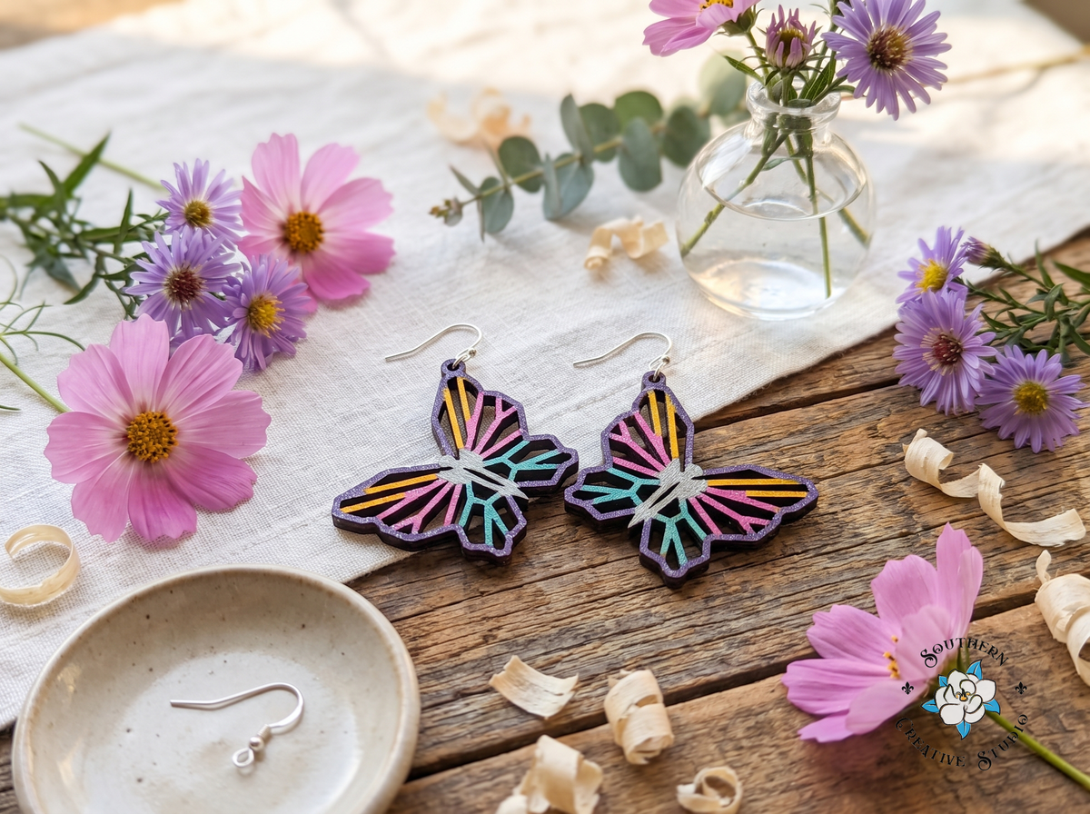 Geometric butterfly earrings with pink cosmos, purple asters and eucalyptus on rustic wood and linen
