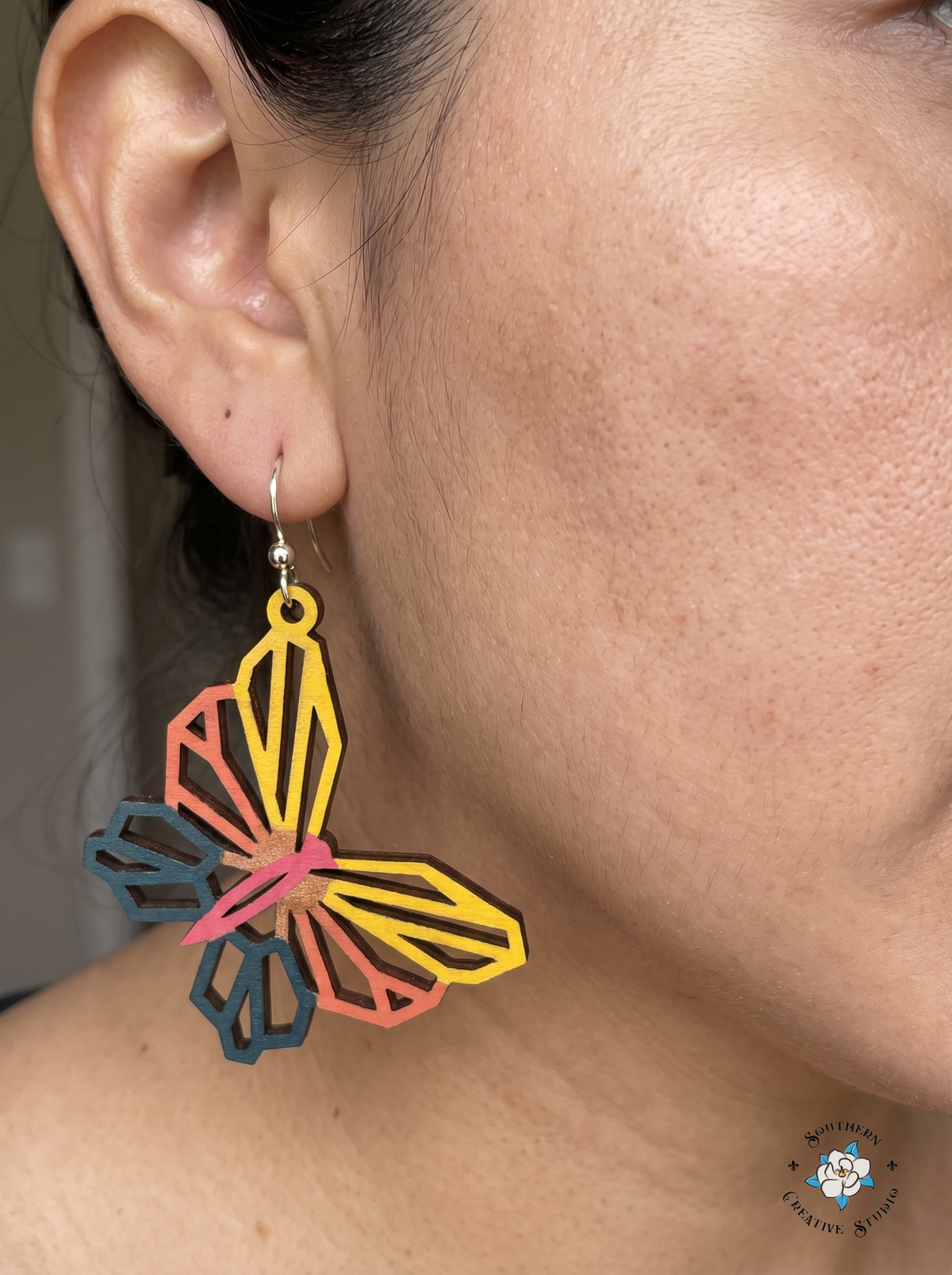 Close-up of woman wearing yellow and coral geometric butterfly wood dangle earring