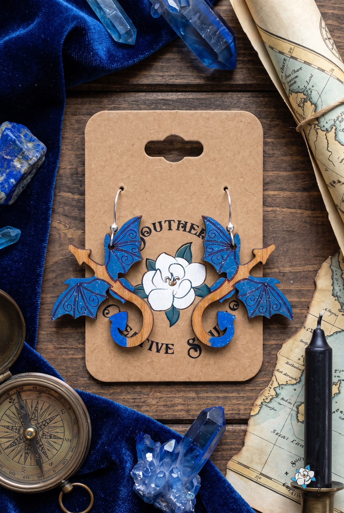 Flat lay of blue dragon earrings on SCS card with blue velvet, lapis crystals, compass and sea chart