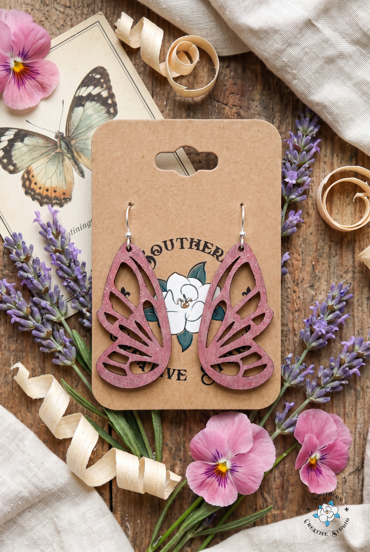 Pink butterfly wing earrings flat lay with lavender and pink pansies