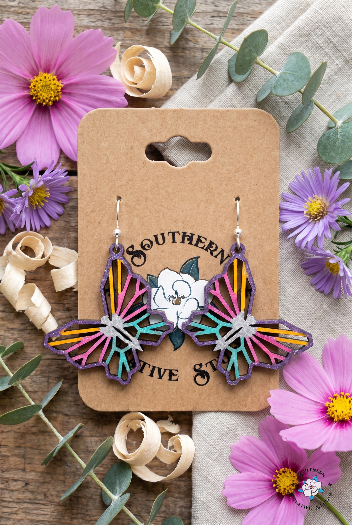 Geometric butterfly earrings flat lay with pink cosmos and purple asters on kraft card