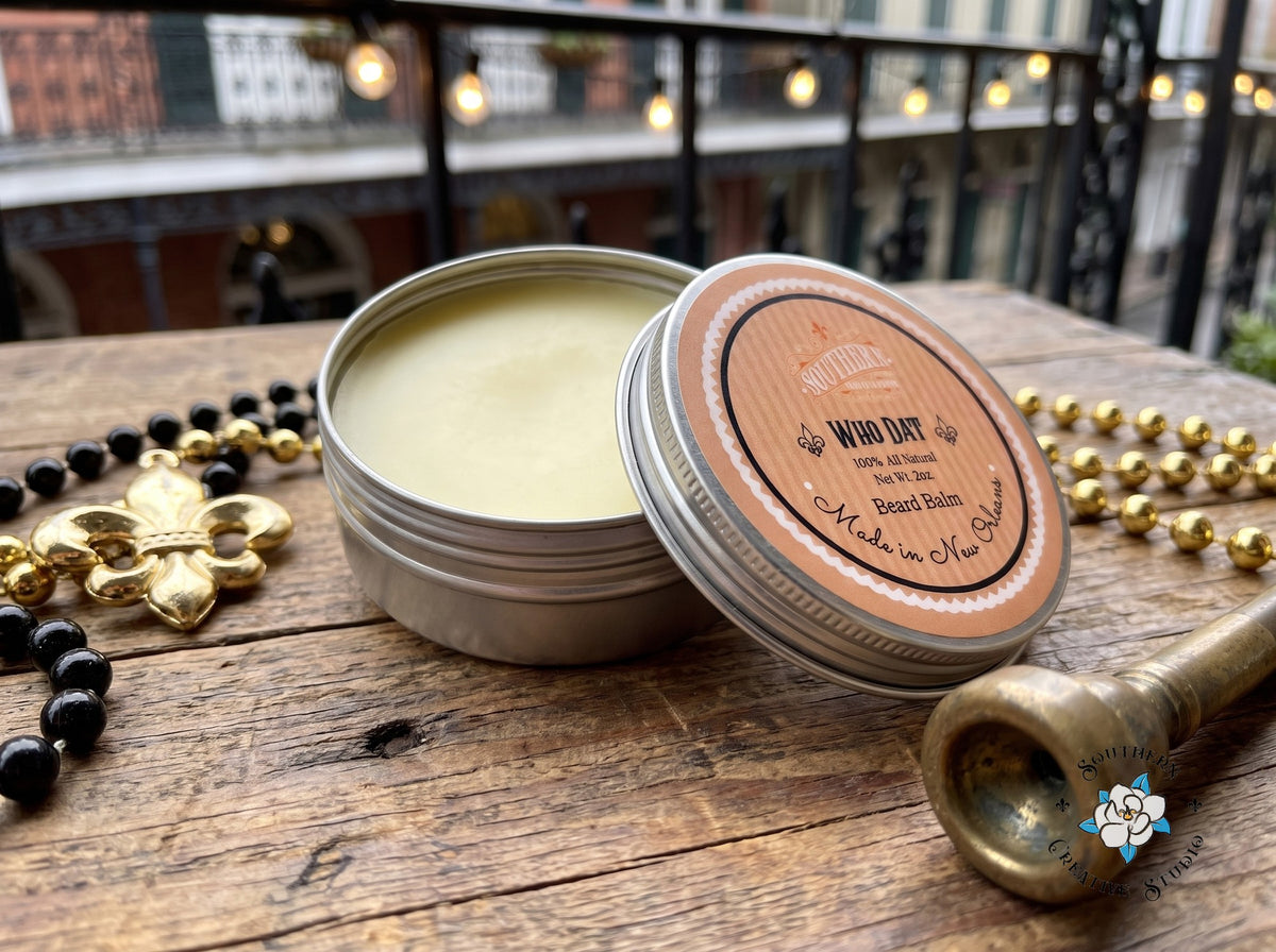 WhoDat beard balm close-up, open tin with leaning lid and black and gold Saints game-day with a fleur-de-lis and beads