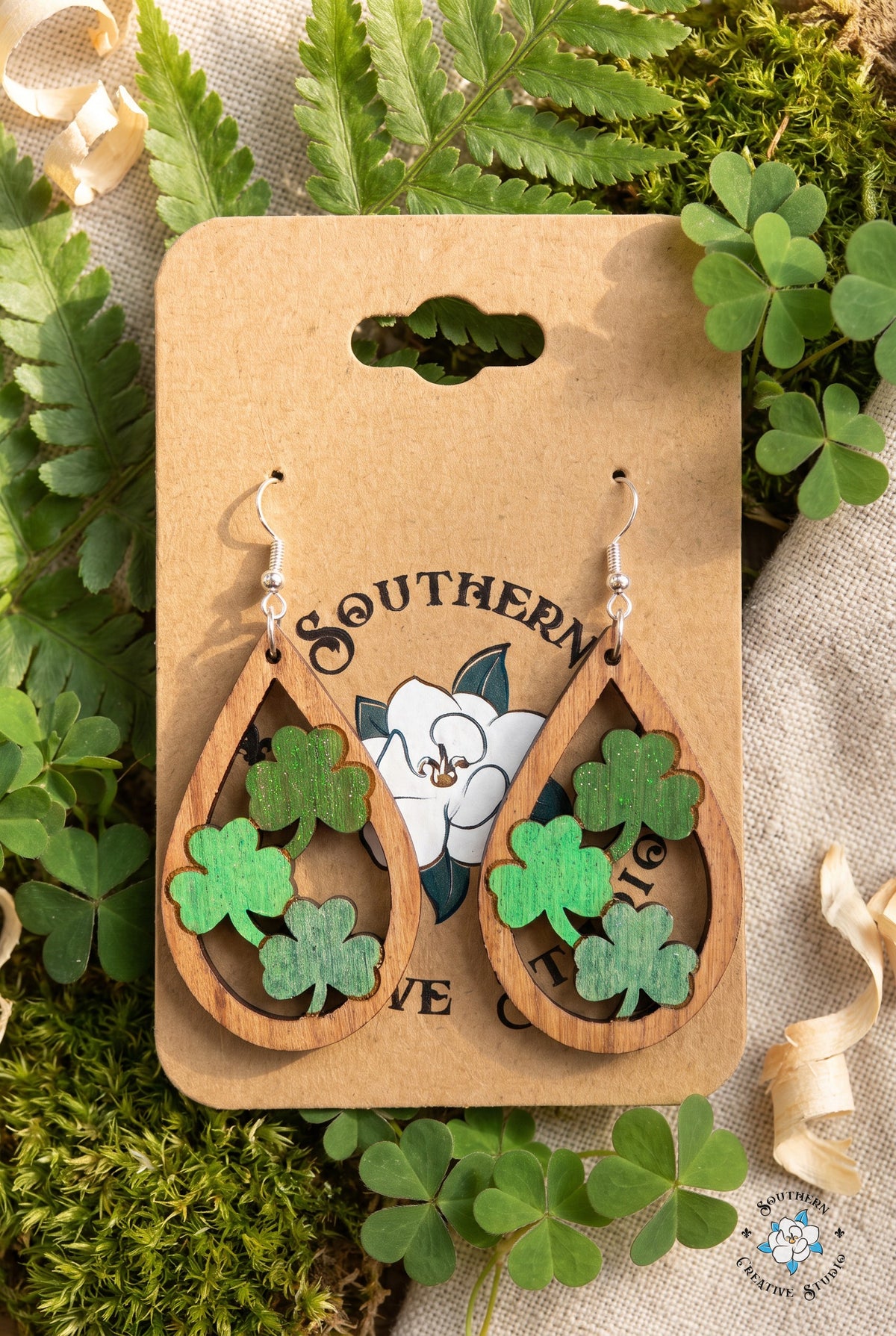 Three clover teardrop earrings on card in a fern and shamrock flat lay