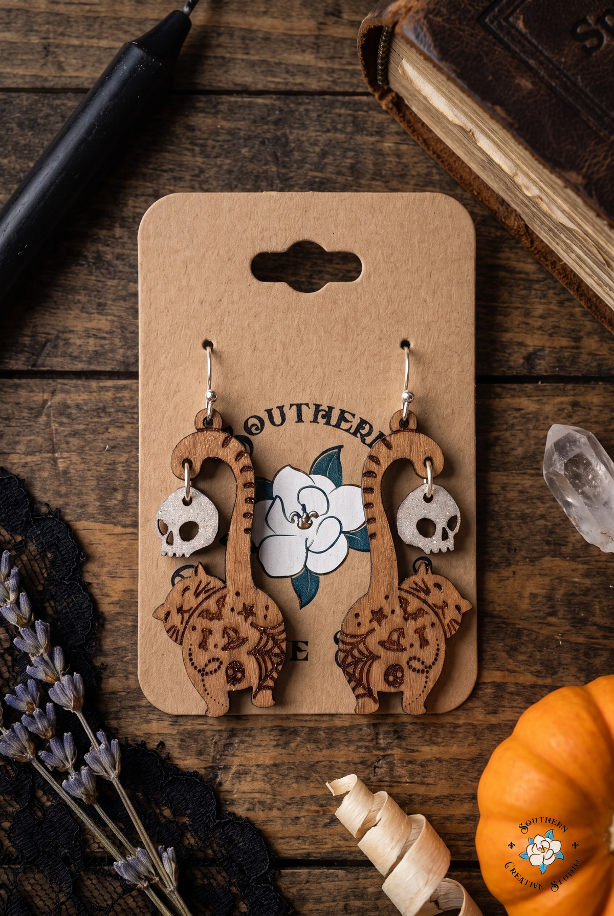 Witchy Halloween flat lay with cat butt earrings on hang card, spellbook, candle and lavender