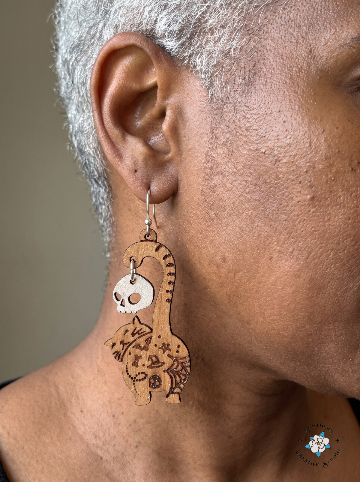 Close-up of woman wearing wood cat butt earring with dangling white skull