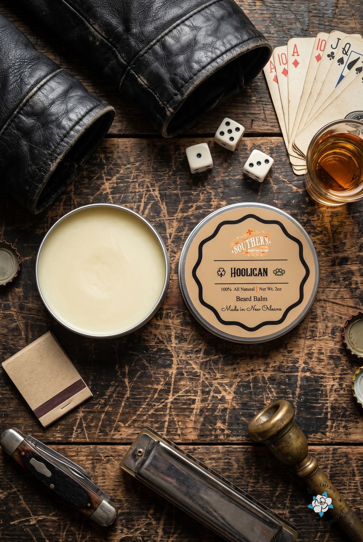 Hooligan beard balm flat lay, open tin and lid with a night-time French Quarter table with dice, whiskey and a brass trumpet mouthpiece