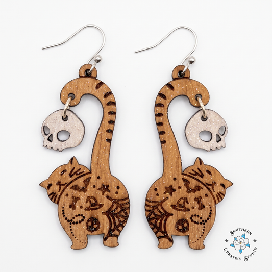 Engraved wood cat butt dangle earrings with white skull on white background