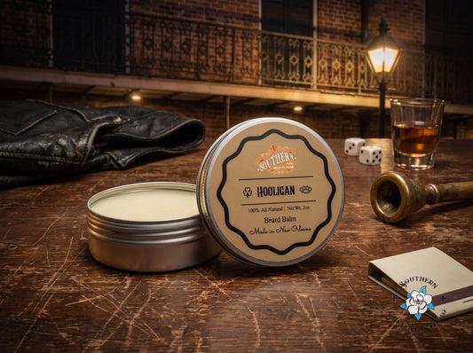 Hooligan beard balm by Southern Creative Studio, open tin and lid with a night-time French Quarter table with dice, whiskey and a brass trumpet mouthpiece