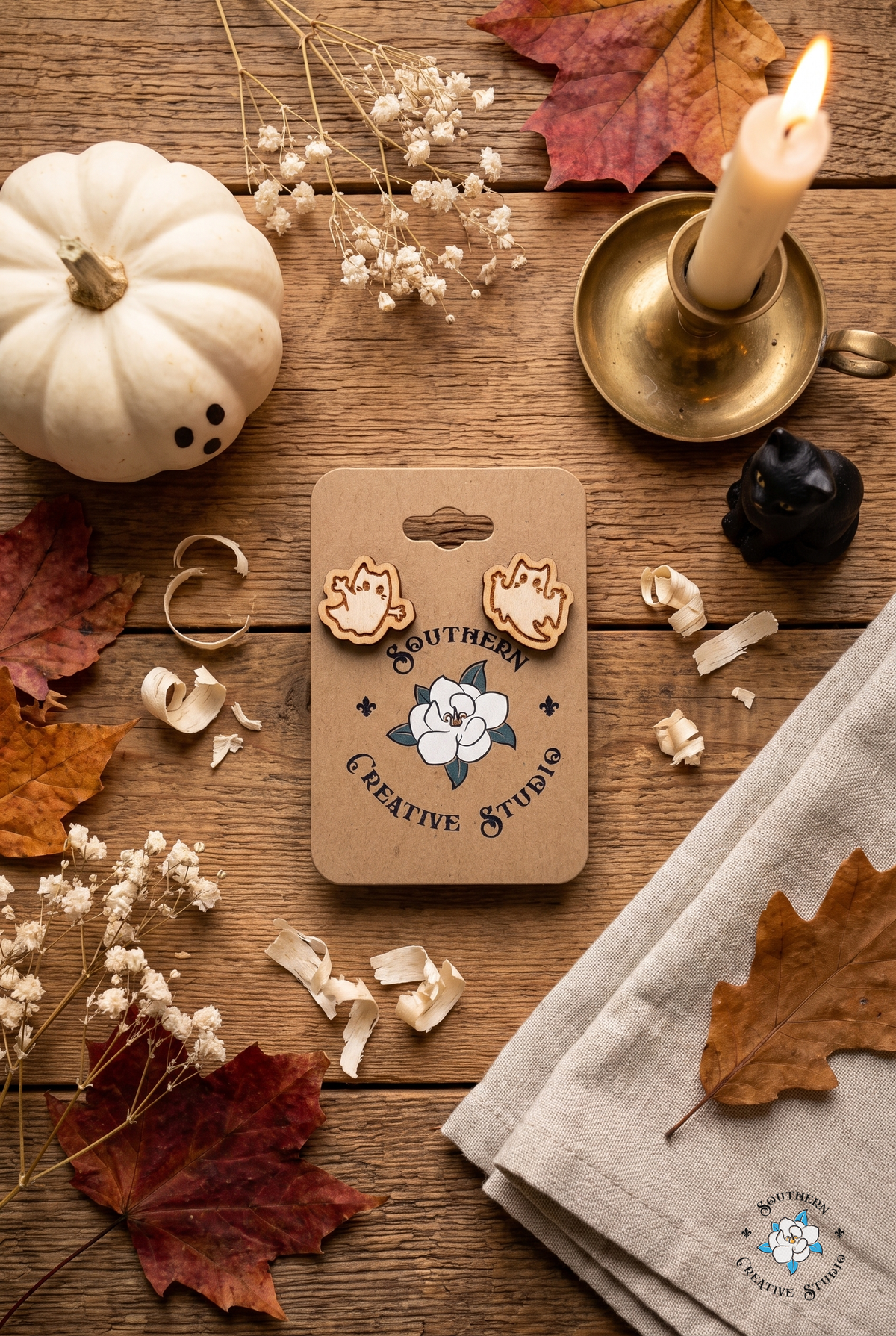 Ghost cat stud earrings on card flat lay with Halloween pumpkin, candle and autumn leaves