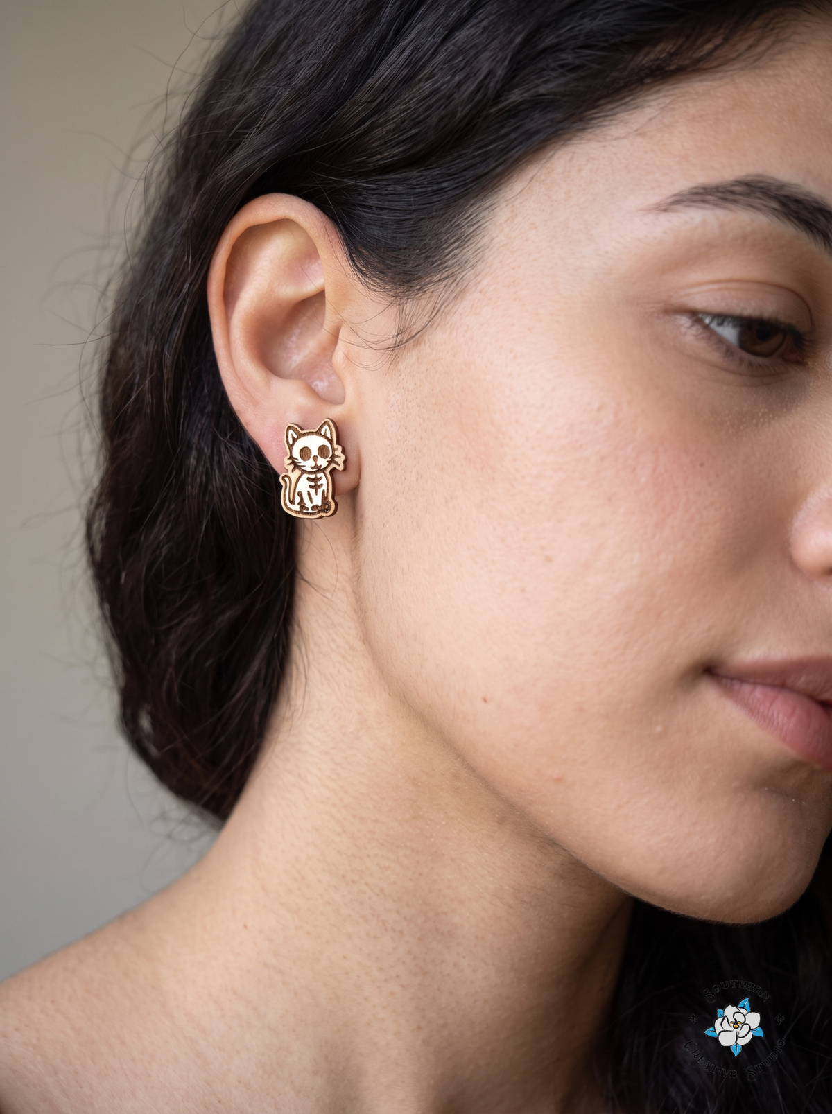 Close-up of white skeleton cat wood stud earring worn in ear