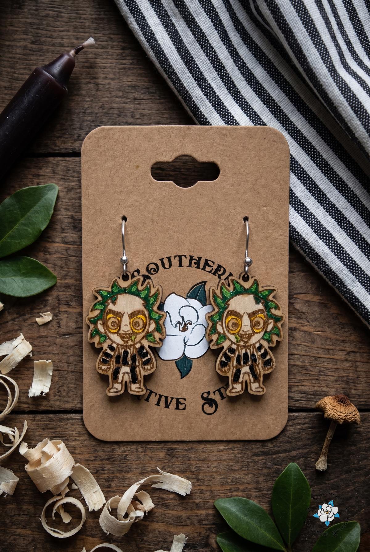 Haunted flat lay with striped suit ghoul earrings on hang card, striped cloth and mushroom
