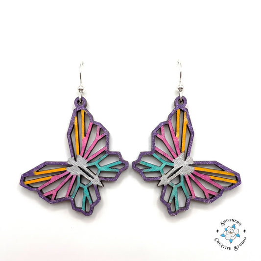 Geometric butterfly earrings, open see-through layered hand-painted wood with purple edge and pink, yellow, teal stripes on white background