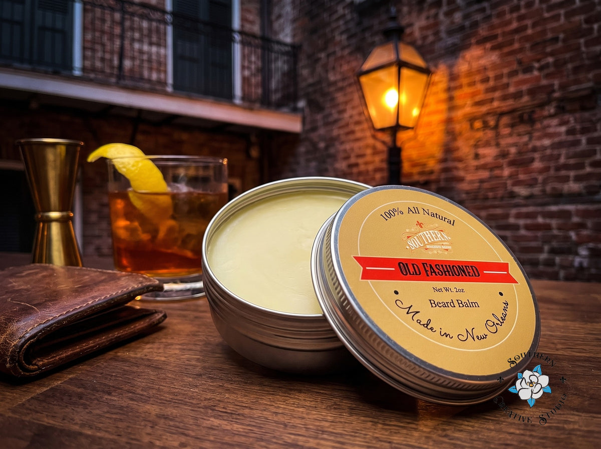 Old Fashioned beard balm close-up, open tin with leaning lid and a French Quarter courtyard bar with a Sazerac-style cocktail and gas lantern