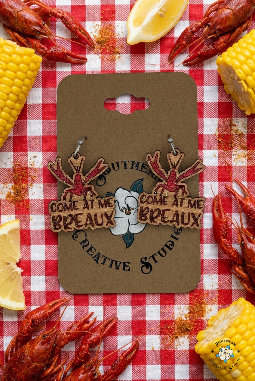 Flat lay moodboard of Come At Me Breaux crawfish hand-painted wood earrings on Southern Creative Studio card with crawfish boil props