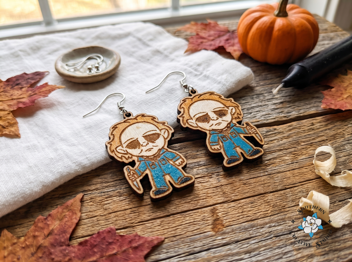 Handmade slasher Halloween earrings on rustic wood with pumpkin, candle and autumn leaves