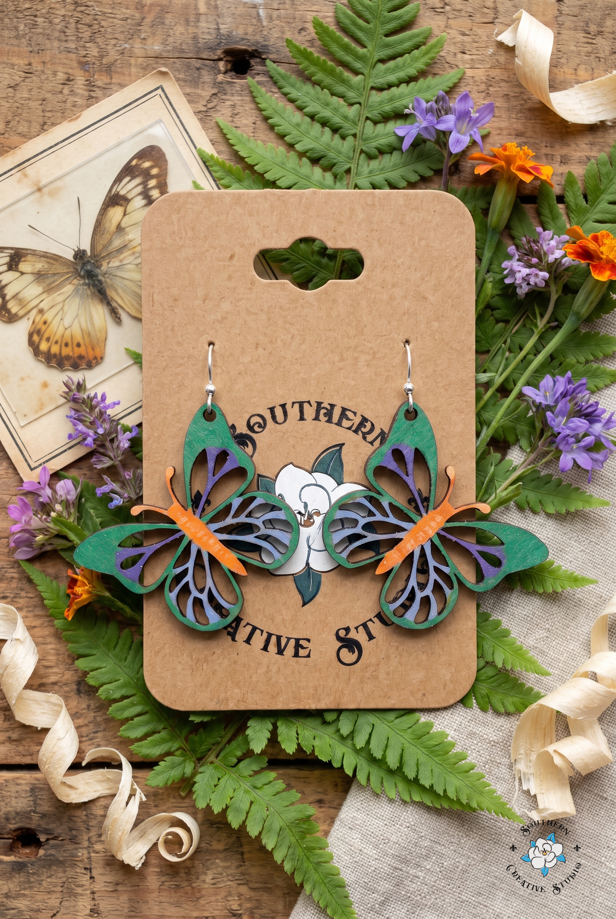 Colorful butterfly earrings flat lay with ferns and wildflowers on kraft card