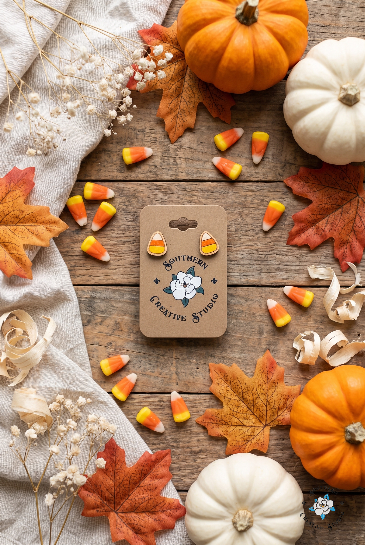 Fall flat lay with candy corn stud earrings, pumpkins and autumn leaves