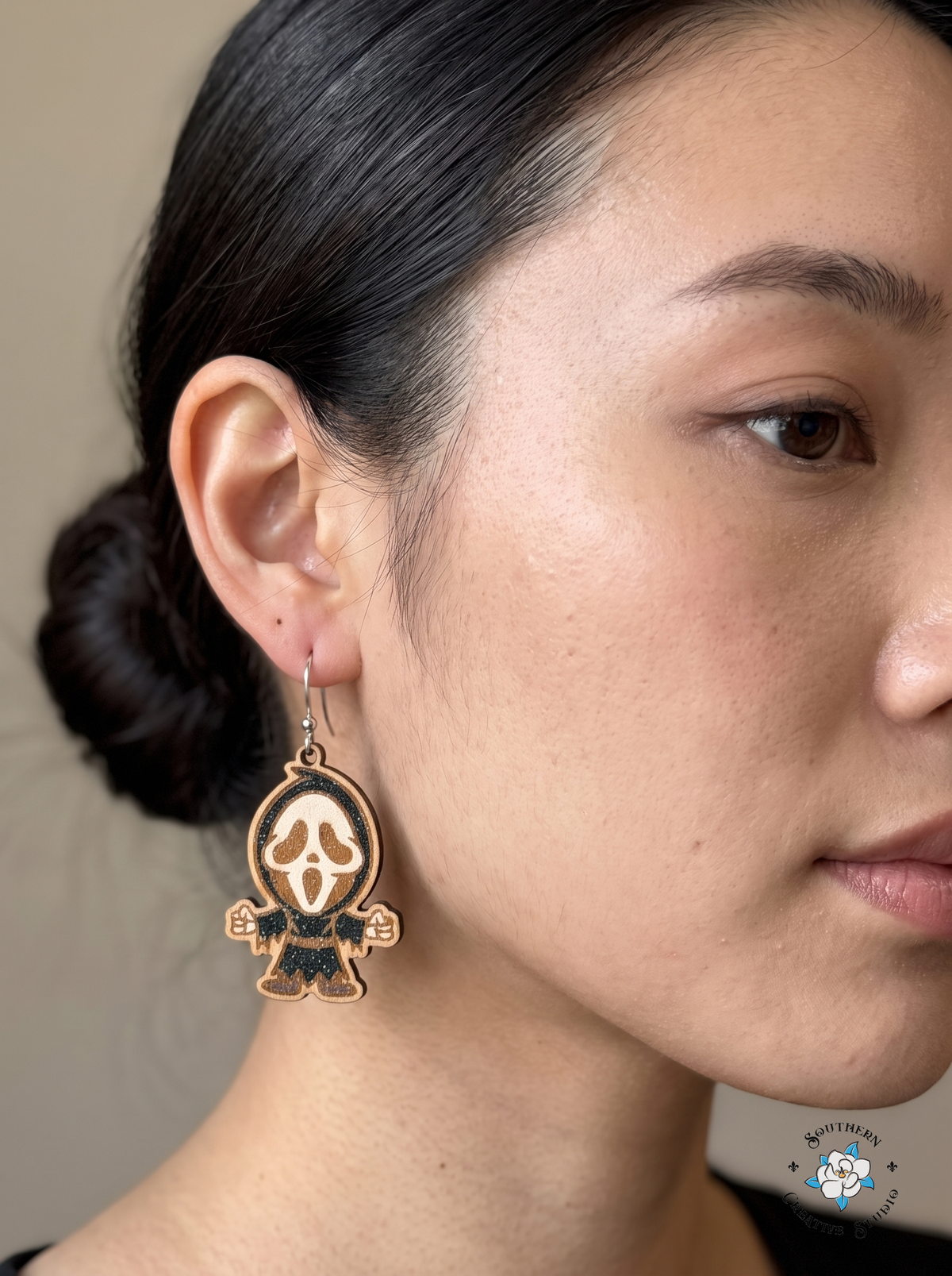 Close-up of woman wearing hand-painted wood screaming ghost mask earring