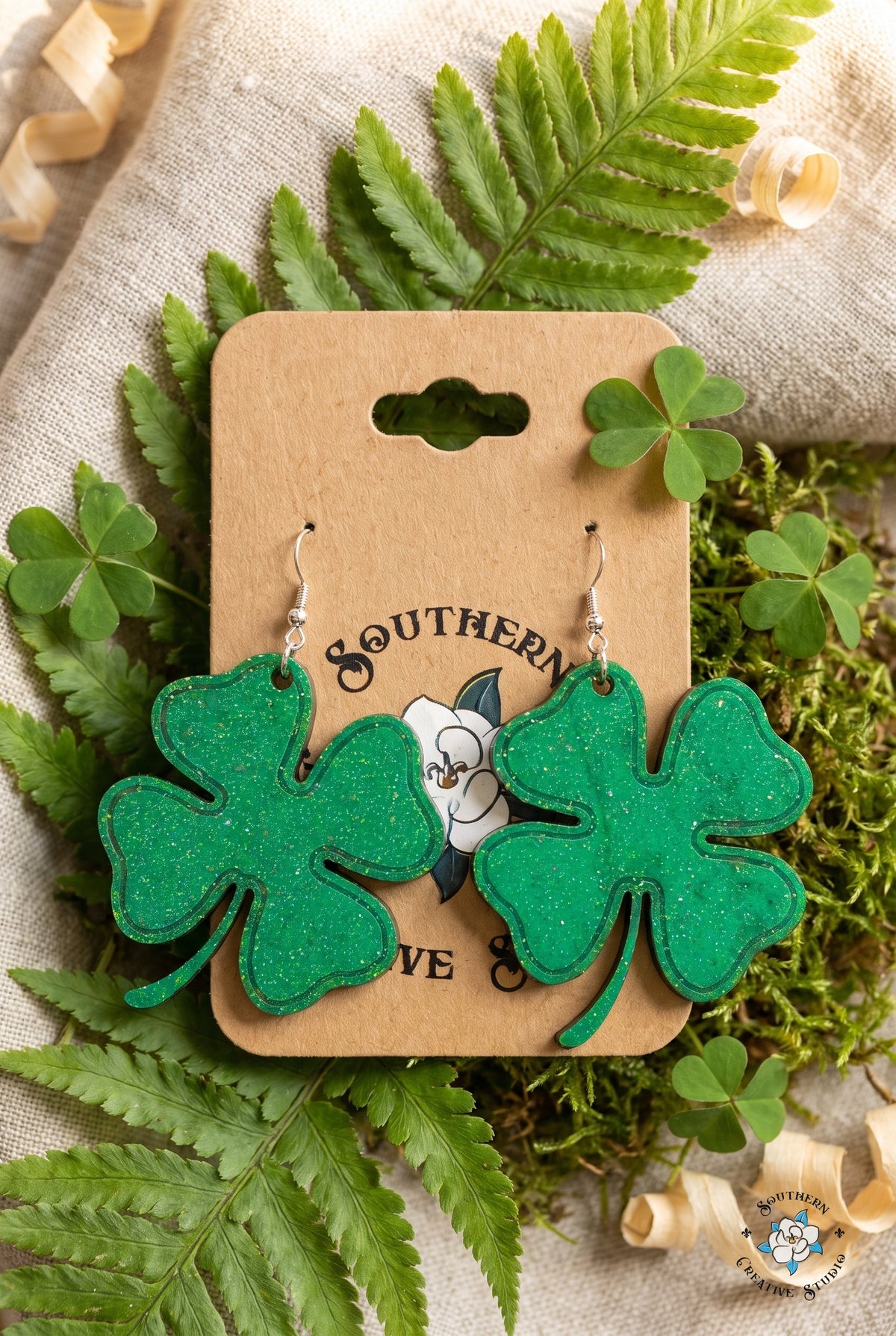 Large four leaf clover earrings on card in a fern and shamrock flat lay