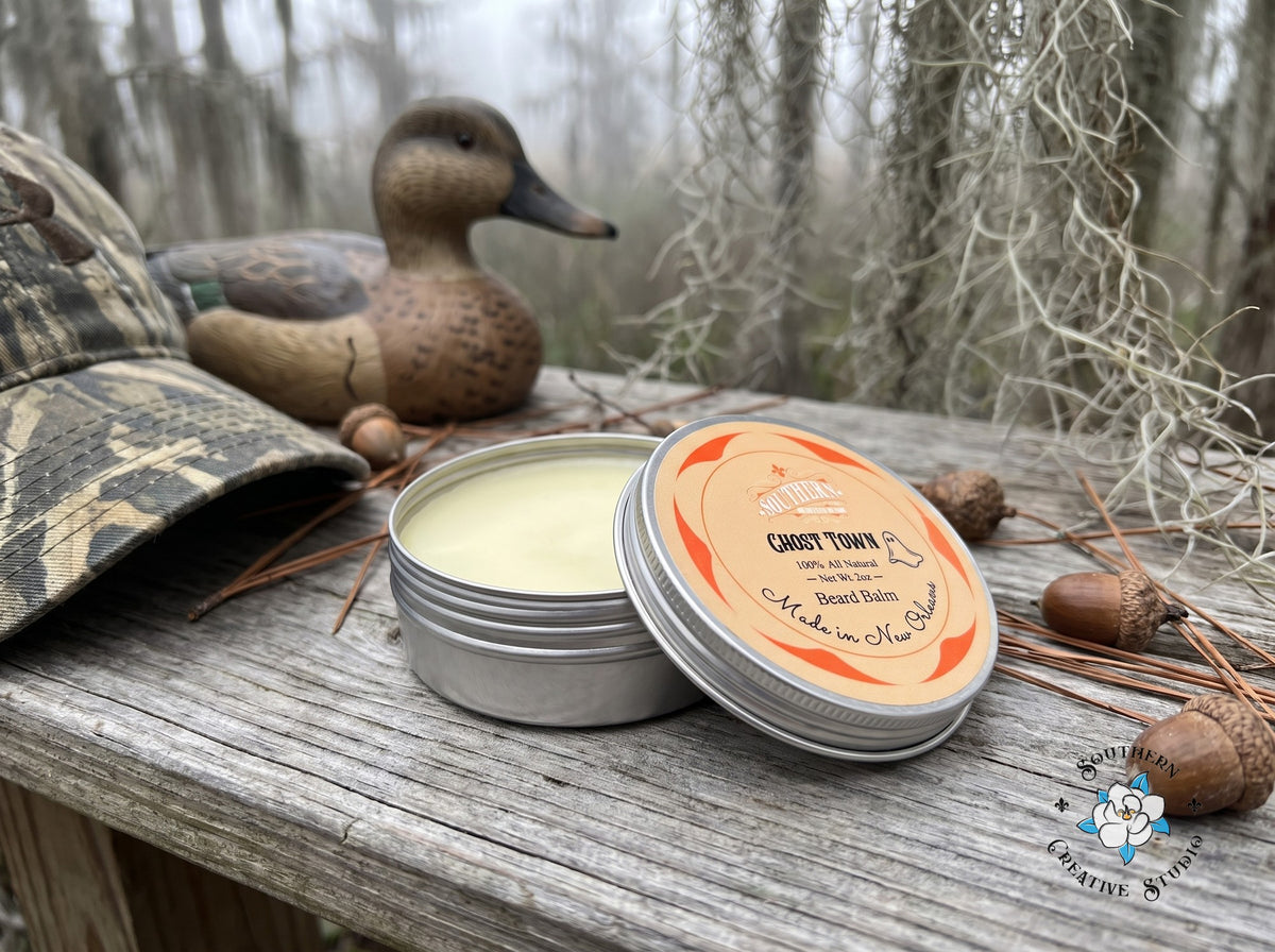 Ghost Town beard balm close-up, open tin with leaning lid and a misty Louisiana marsh with camo, a duck decoy and Spanish moss