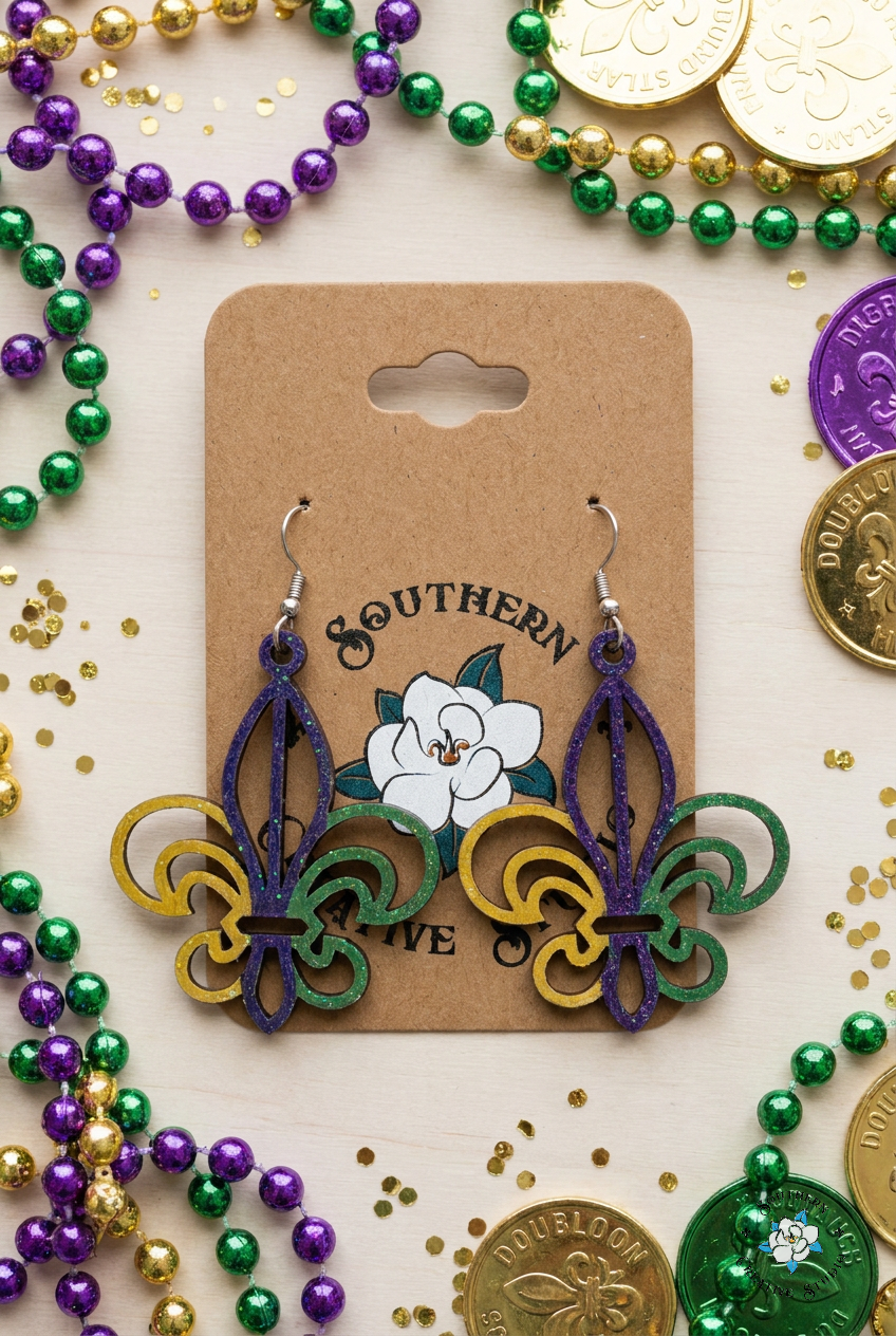 Flat lay moodboard of Mardi Gras Fleur-de-Lis hand-painted wood earrings on Southern Creative Studio card with carnival props